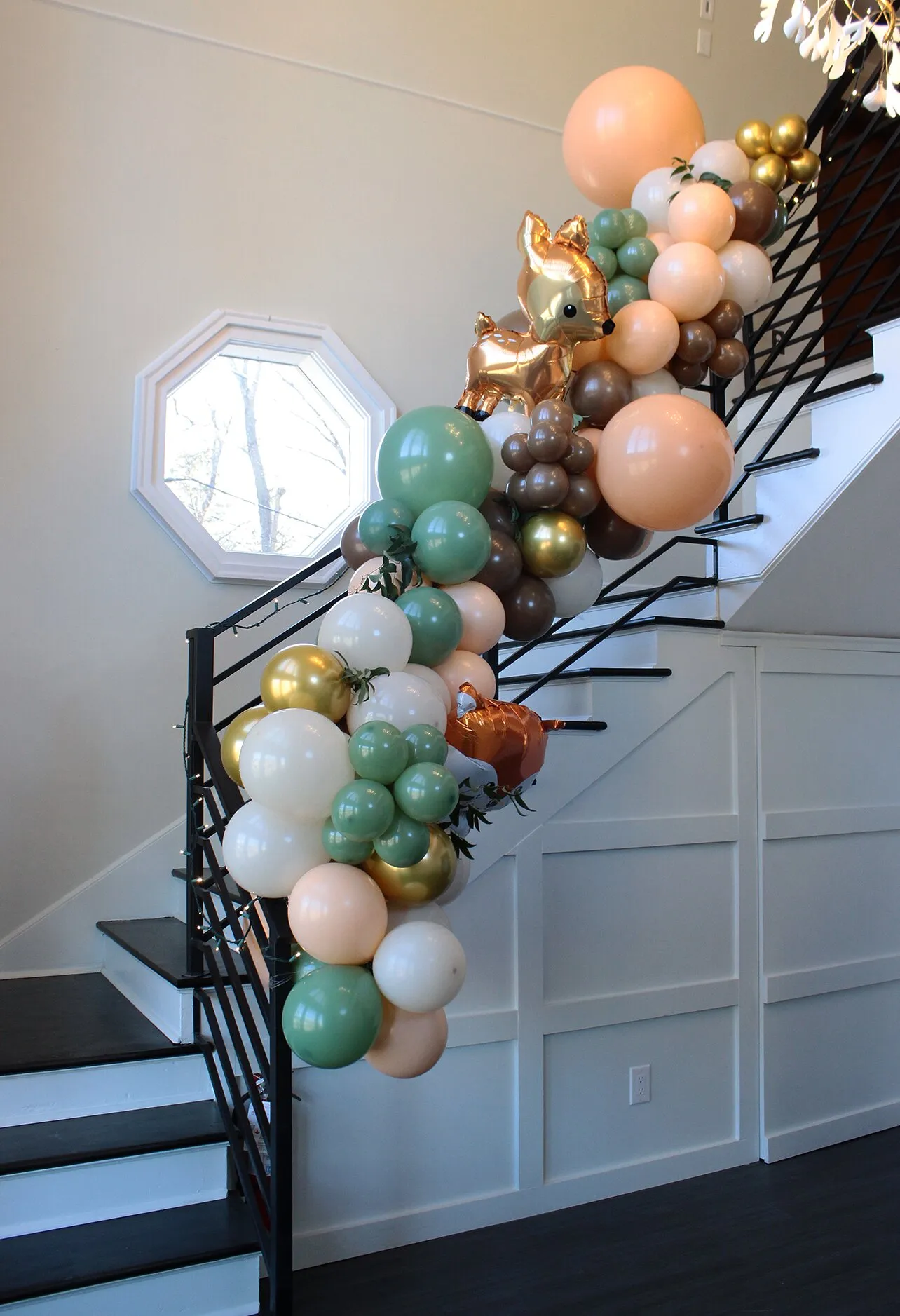 The foyer's main staircase with a black railing and white paneling, dressed with a balloon garland for an event